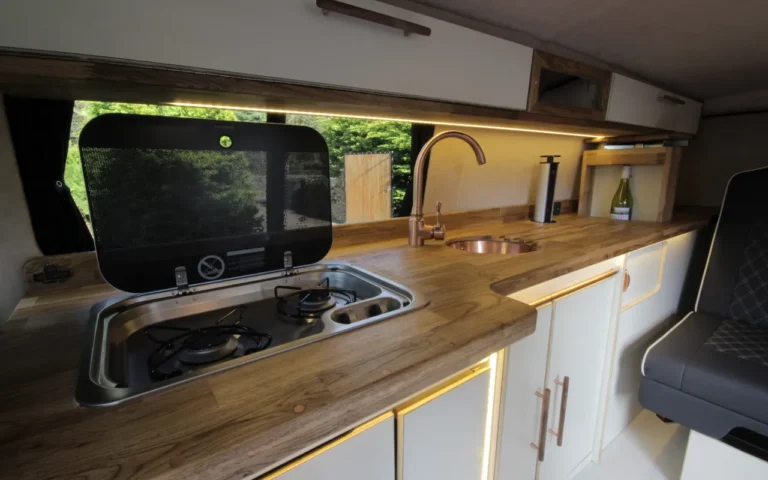 A campervan interior with a wooden countertop, sink, stove and cabinets