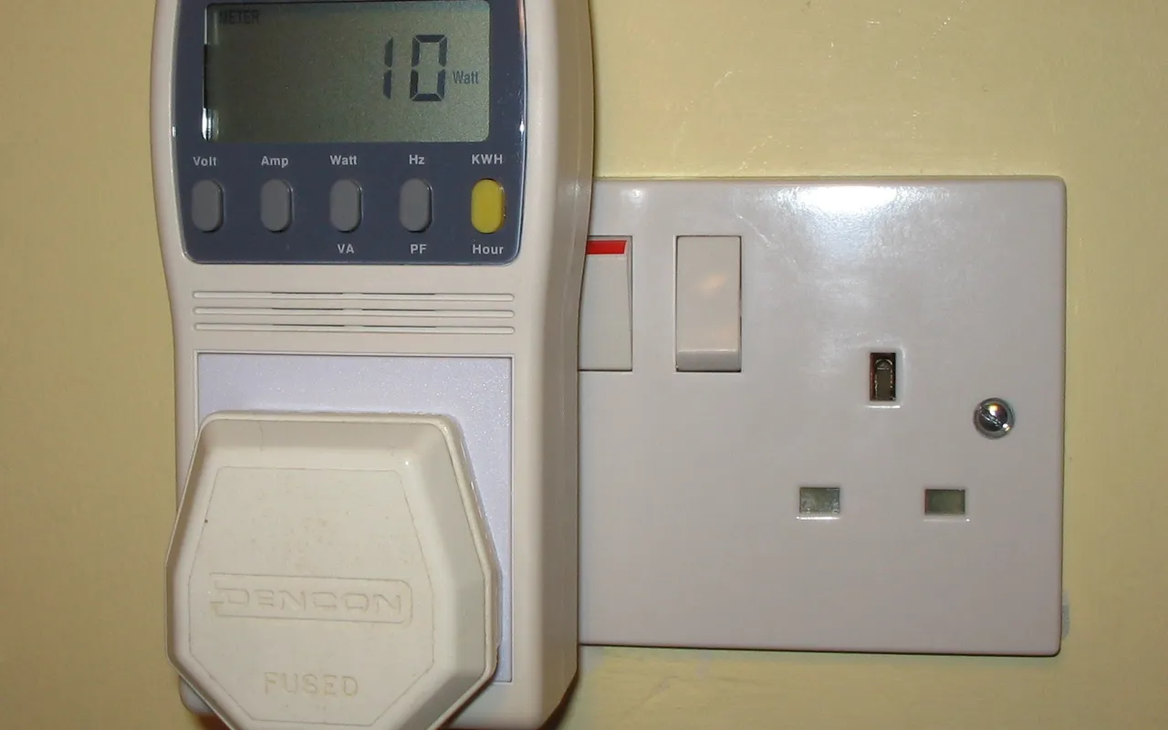 A plug-in power and energy monitor showing a wattage reading