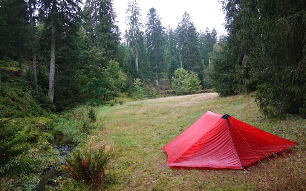 A small red tent pitched in a forest clearing at a trekking camp