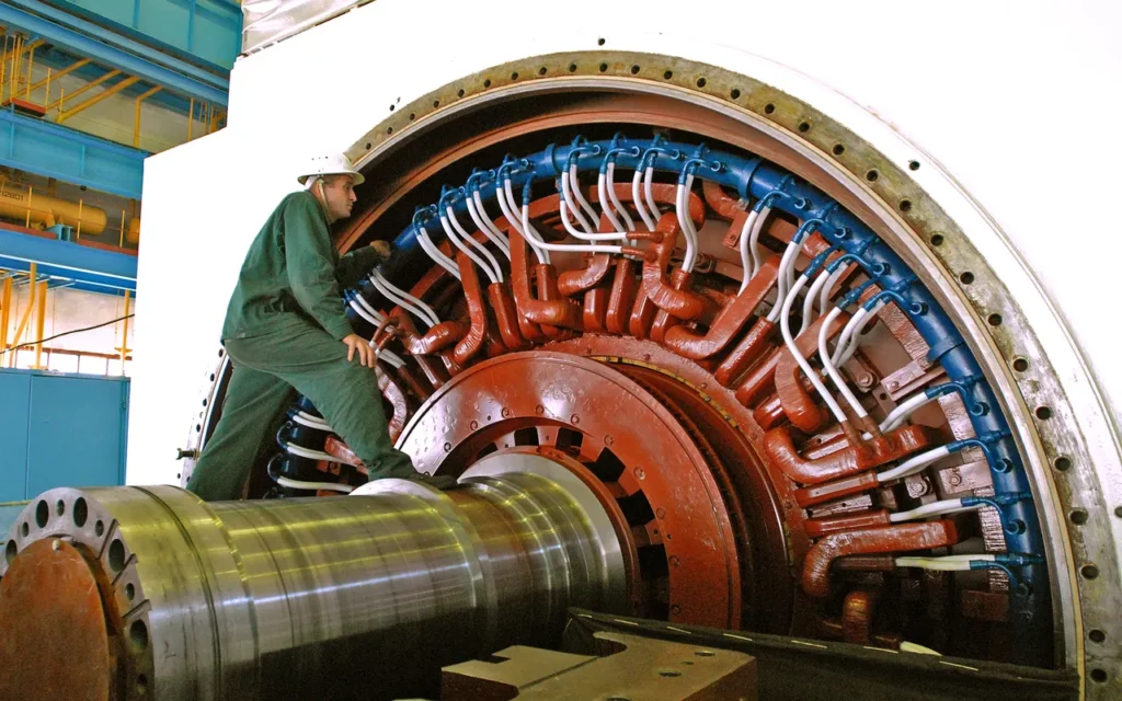 A worker beside the stator windings and rotor shaft of a large electrical generator