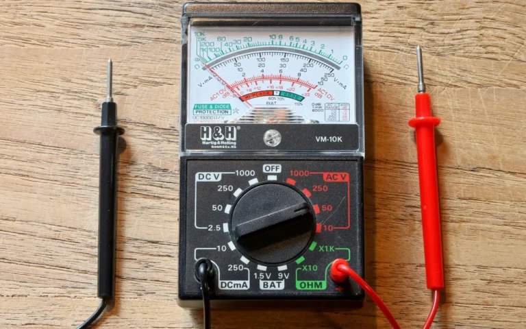 An analog multimeter with red and black test leads on a wooden surface