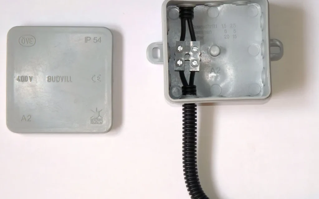 An electrical junction box with its cover removed beside the closed cover, showing wire connections