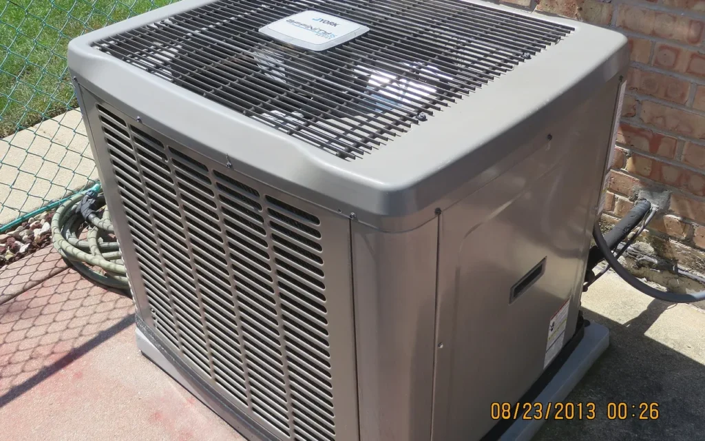 A central air conditioning condenser unit on a pad beside a brick house