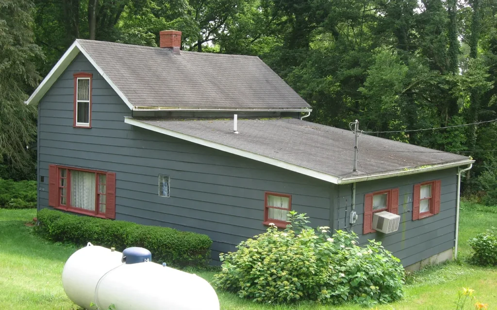 A white residential propane tank on the lawn beside a small gray house