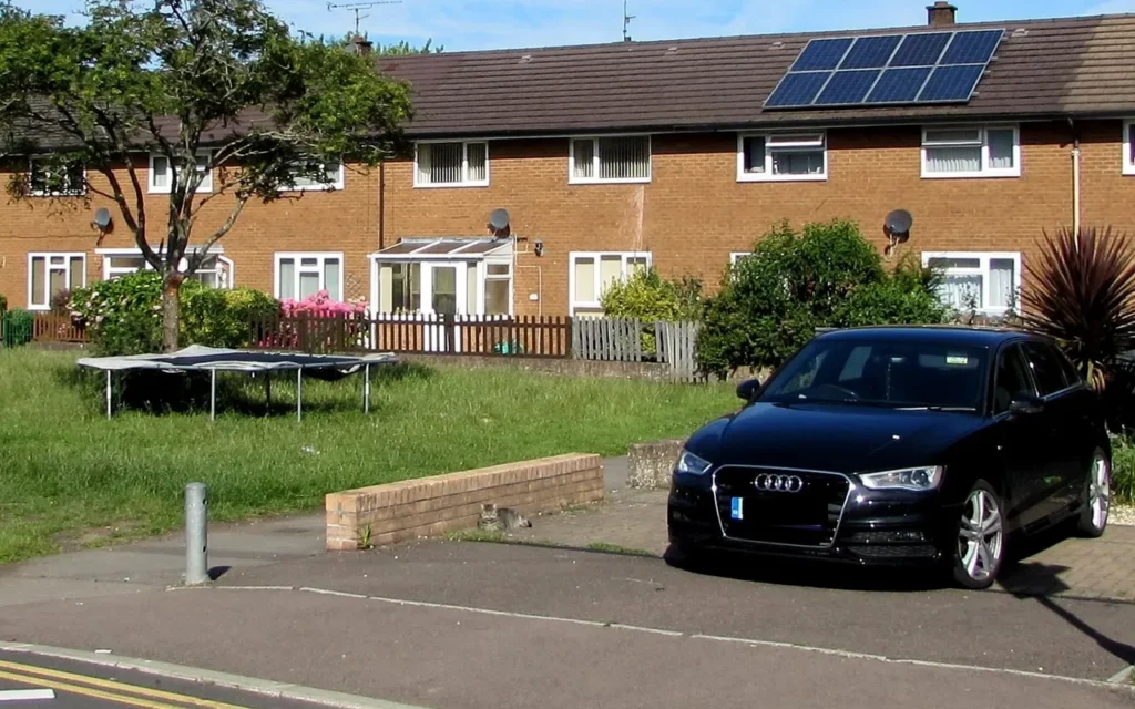 Rooftop solar panels on a row of brick houses with a car parked in front