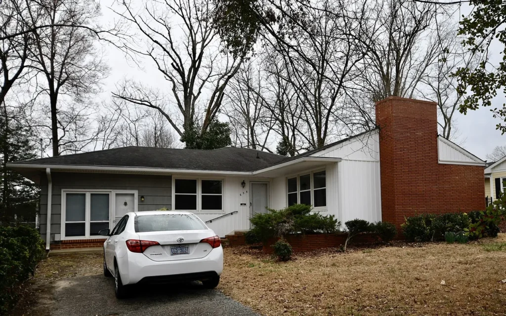 A single-story house with a brick chimney and a car parked in the driveway