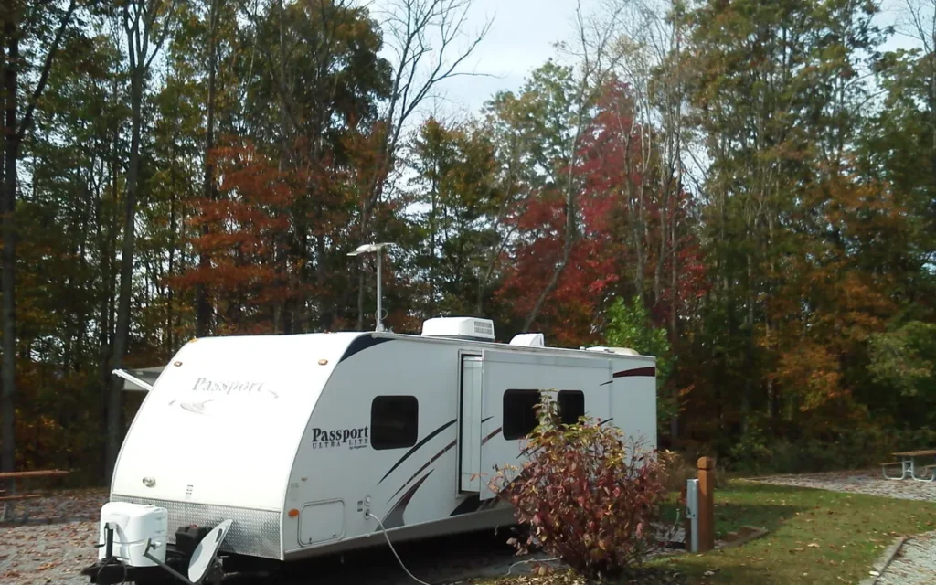 A white travel trailer parked at a wooded campsite in autumn