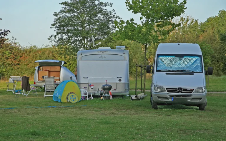 Two caravans and a camper van set up on a grassy campsite with an awning and chairs