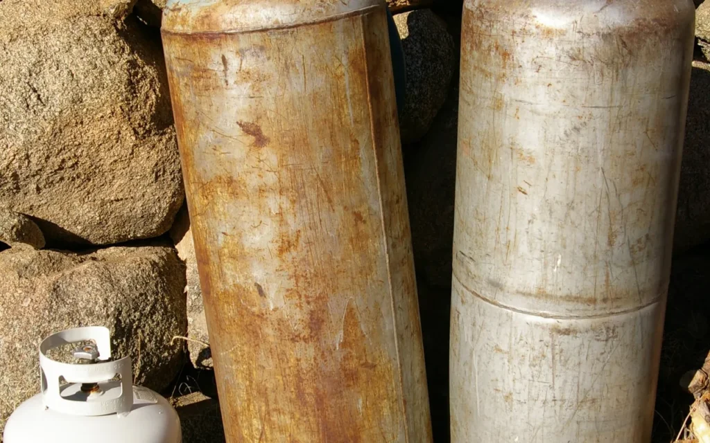 Two large propane cylinders, one with a regulator and hose attached, beside a smaller 20 lb tank