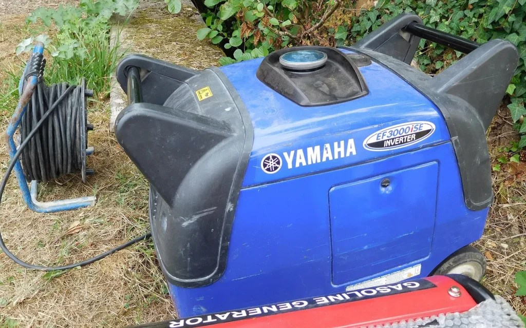 A blue Yamaha inverter generator sitting on grass beside an extension cord reel